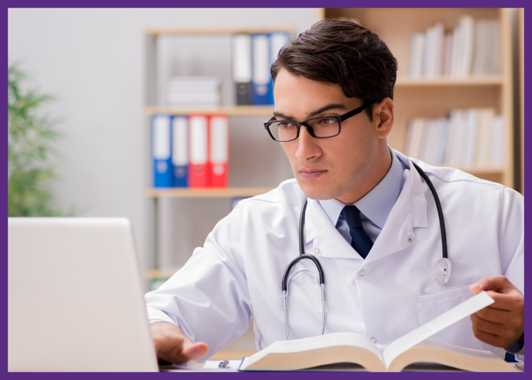 photo of a doctor studying, looking at his computer with a text book open on his desk- it might be Time to Change Doctors if your doctor doesn't have the knowledge or experience for your condition