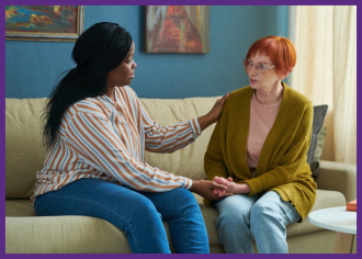 photo of a social worker comforting a senior woman as they both sit on a sofa