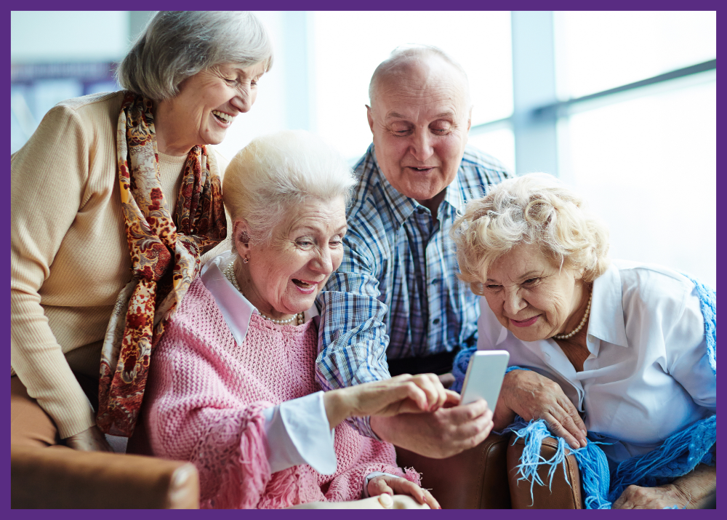 photo of 4 well dressed seniors sitting together looking at a phone