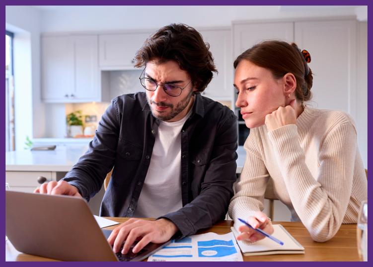 photo of a couple sitting at a table, looking at a laptop, worrying about bills that are on the table - financial strain often adds to caregiving stress