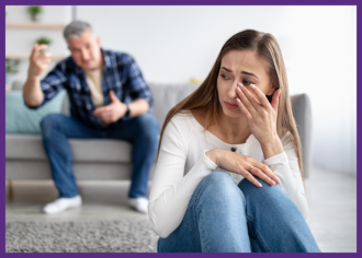photo of a woman sitting on the floor, crying, while her husband yells at her from the sofa